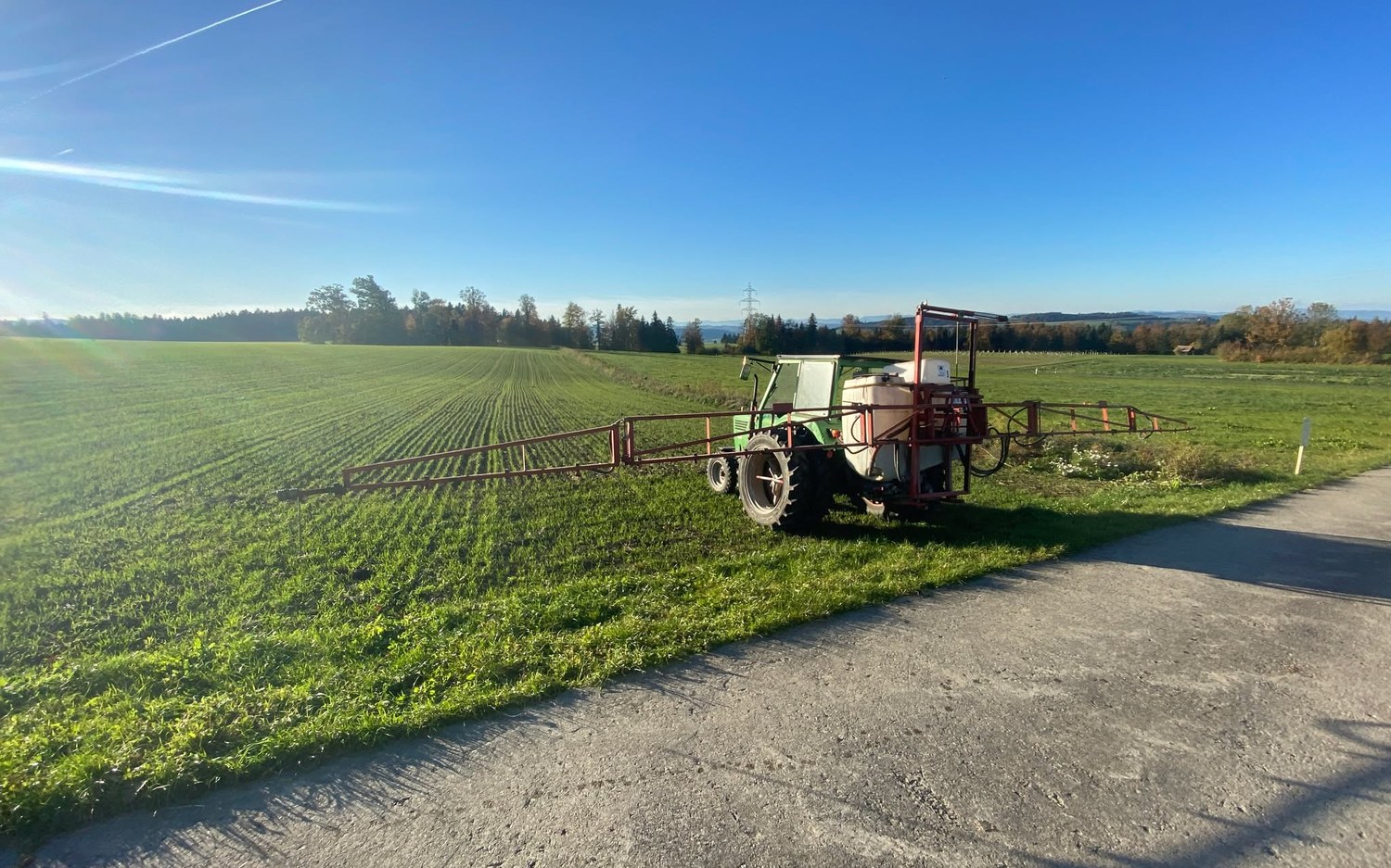 Traktor mit Feldspritze am Rand eines Winterweizenfelds im November
